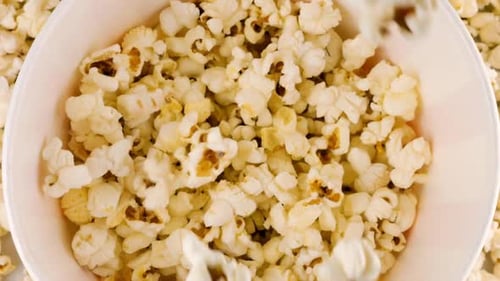 Popcornkörner, die in einen rot-weiß gestreiften Eimer fallen, auf dem Hintergrund Popcornkörner