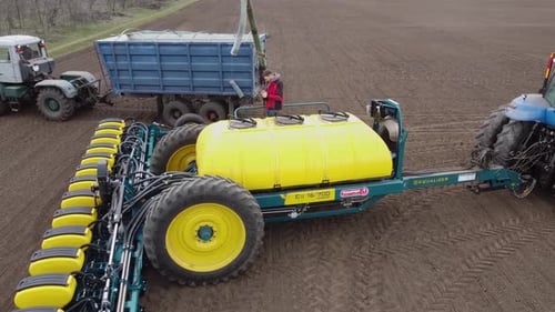Blue tractor with yellow seeder working on the field in Ukraine OA