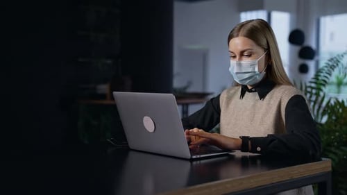 Woman Wearing Mask Typing on Laptop in Office