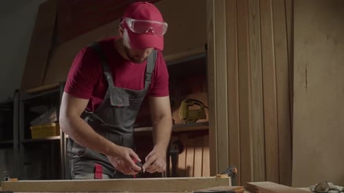 A Skilled Craftsman is Carefully Measuring the Length of a Wooden Board with a Tape Measure Inside a