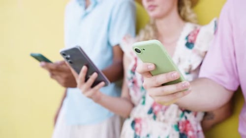 Young Adults Using Mobile Phones Against a Colorful Wall