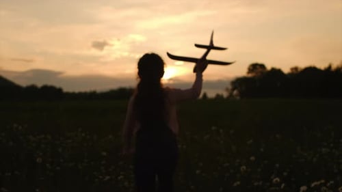 Silhouette of little girl kid runs across beautiful summer field on mountains background
