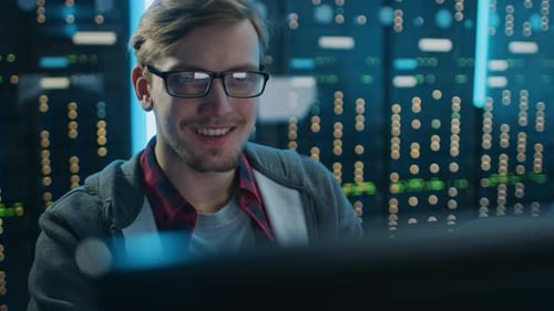 Smiling man works on computer in server room