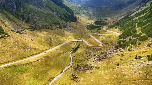 Winding mountain road flowing in the valley along with stream.