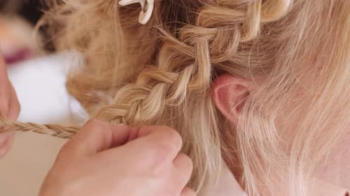 Woman weaving herringbone braid for blonde hair bride getting ready