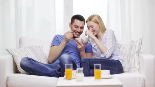 Happy Couple Eating From Same Bowl on Couch