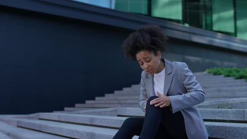 Businesswoman Sitting Outside Massaging Sore Knee in Pain