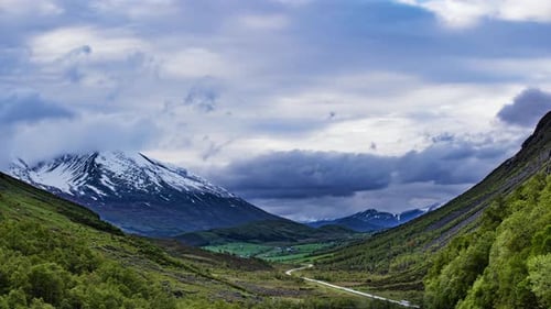 Norwegian landscape in summer. Clouds passing over the mountains, forest, and a narrow road stretchi