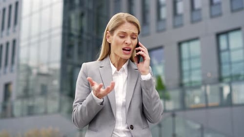 Angry businesswoman arguing while talking on smartphone standing on the street near an office