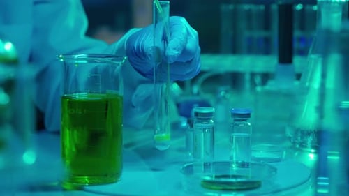 A Woman Scientist Pipettes a Green Liquid Into a Test Tube with White Powder