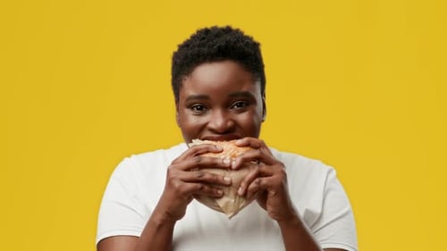 Young African American Woman Enjoying a Burger in Studio with Vibrant Background