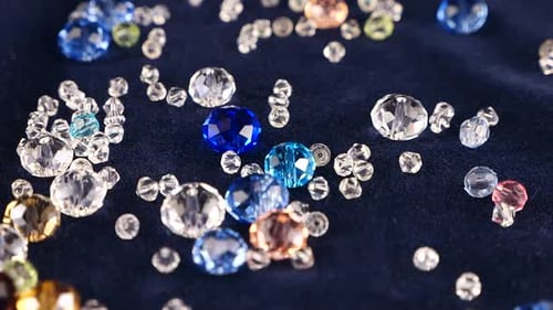 Multi-colored transparent jewelry crystals and rock crystal fall on blue velvet. Slow motion.