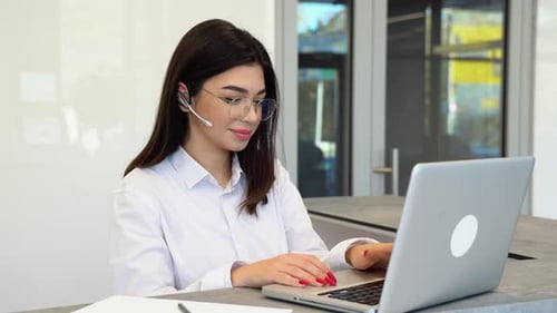 Female Customer Support Operator with Headset Uses a Laptop