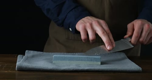 Man sharpening knife with sharpener at wooden table against black background, closeup