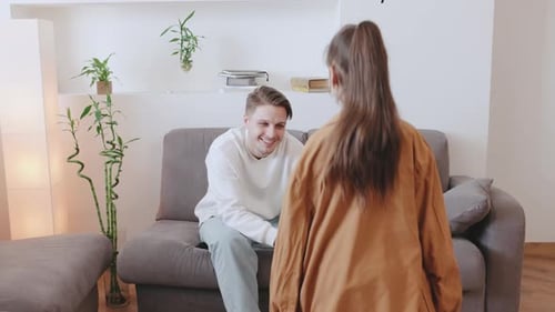 Child Wears a Brown Jacket and Spins Around While an Adult Sits on a Couch in a Welllit Room with