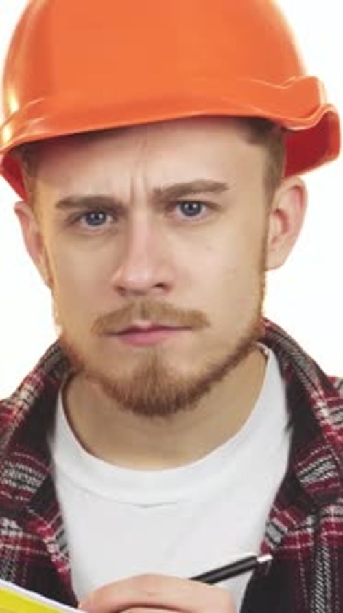 Dedicated Young Male Architect in an Orange Hardhat Meticulously Taking Notes