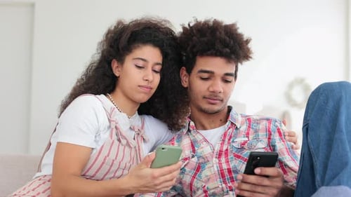 Loving Couple Relaxing Together Using Mobile Phones Indoors