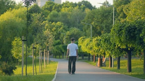 Teen Boy Walks Alone Down City Park Path at Golden Hour