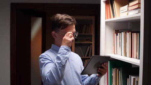 Librarian Using Tablet and Consulting Book Catalog in Library Bookshelf