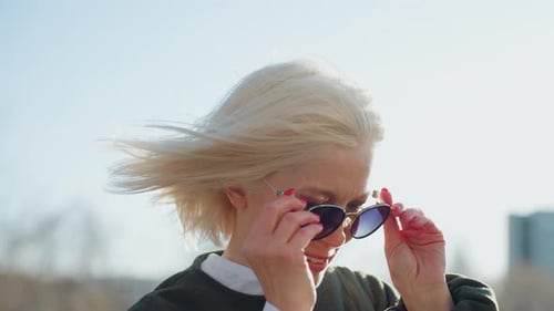Blonde Woman Puts on Sunglasses on Windy Day