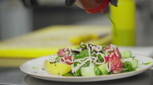 Closeup of a Cook Pouring Green Sauce on a Salad Before Serving in the Kitchen in a Restaurant The