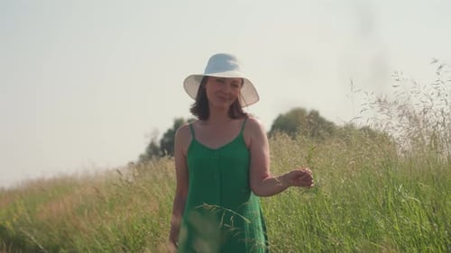 Lady Standing in Sunny Barley Field Touching Plants with Calm Expression