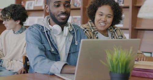African American Students Using Laptop Looking at Screen and Talking Studying in University Library