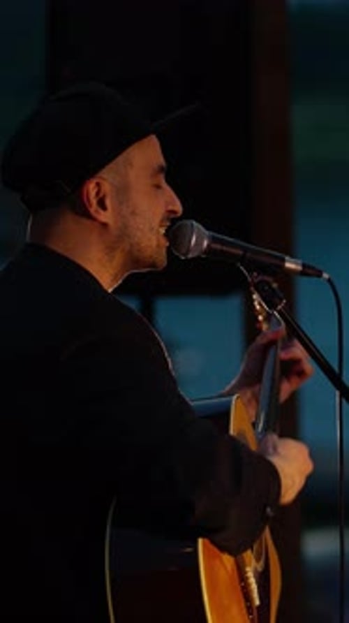 Male Singer Playing Acoustic Guitar on Dimly Lit Indoor Stage