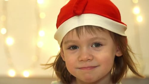 Joyful Child in Santa Hat Smiles with Christmas Lights