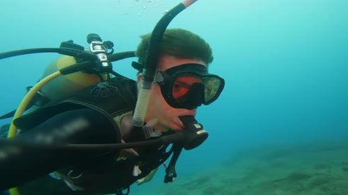Diver in Wetsuit and Large Goggles Swims Slowly Underwater