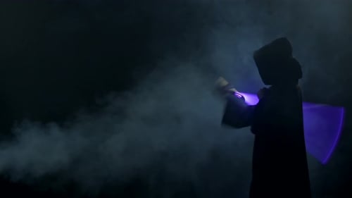 Young Man in Jedi Cosplay Costume with Lightsaber Battle on Black Background in Smoke and Rain Slow