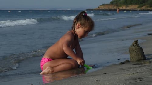Niño jugando a la arena en la playa. Niña construye un castillo de arena sola en la orilla del mar