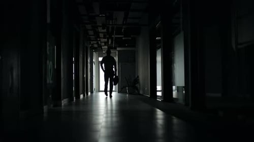 Businessman Walking Down Dark Office Hallway