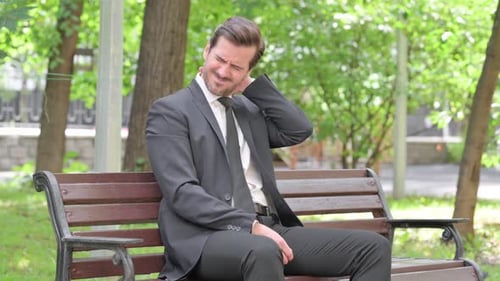 Man in Suit on Bench Rubbing Neck