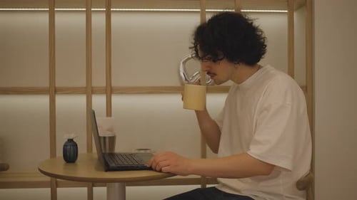 Successful Young Man Using Laptop and Drinks Coffee While Sitting in Cafe in the City Centre