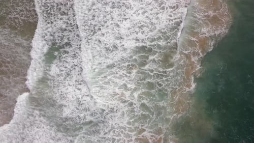 Stormy sea with waves breaking, white foam and beach sand dragged into the sea