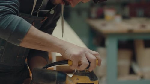 Man Sands Wood in Workshop with Power Sander