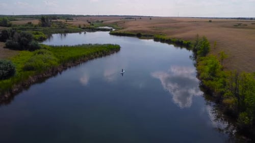 A Young Woman in a Black Bikini Floats on a SUP Board Across a Lake Captured By a Drone