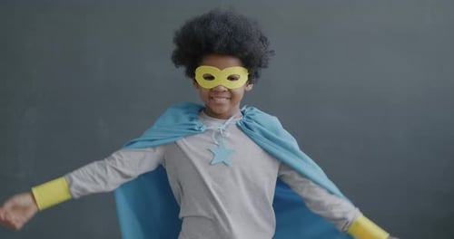 Slow Motion Portrait of Funny African American Child Wearing Super Hero Cape and Mask Showing Biceps