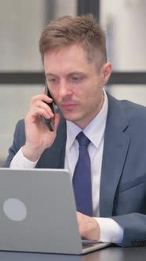 Businessman Talking on Phone While Working on Laptop