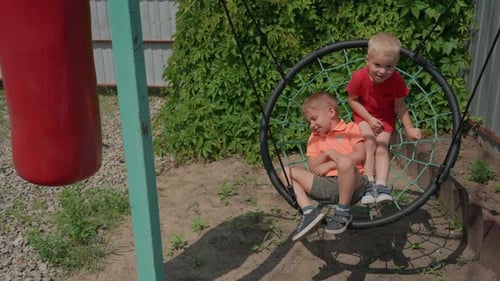 Child Helps Companion On Swing Amidst Sunny Garden Setting Young Boy Cooperates With Friend By