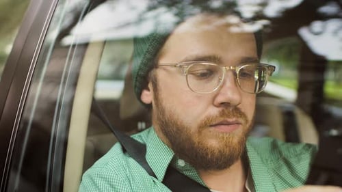 Portrait of Stylish Young Man Riding in a Car, Sitting on a Passenger Seat Uses Smartphone, types M