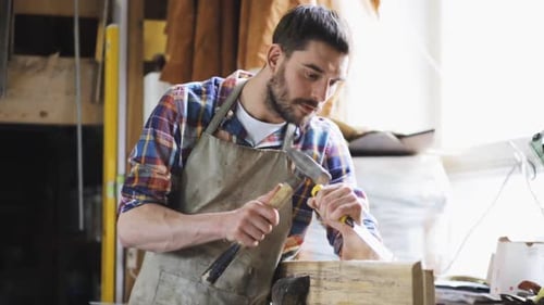 Concentrated man using chisel and hammer in workshop