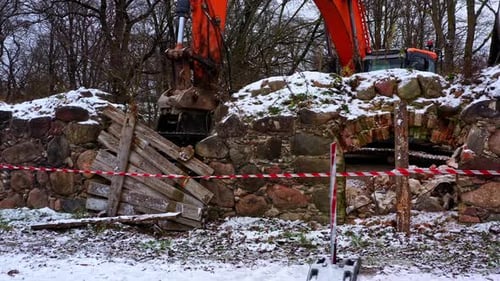 Excavator demolishing old stone structure during winter