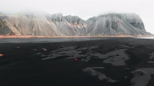 Cinematic 4K Aerial video of a mountain in Iceland with a man walking on the Black Sand Beach