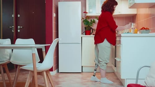Beautiful Happy Woman with Bionic Prosthetic Leg Enters Bright Kitchen to Drink Water and Check
