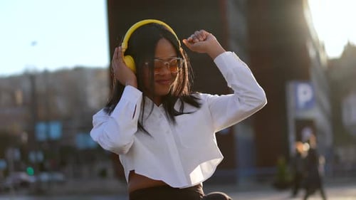 African american woman listening to music with headphones at sunset in the city, dancing