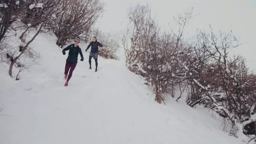 Active caucasian couple trail running together through a snowy forest in Canada