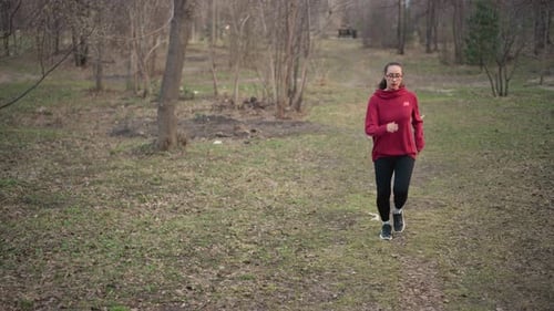Young Woman Runs Through Park in Red Sweatshirt