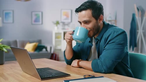 Handsome Young Man Works on a Laptop While Sitting at His Desk in the Cozy Living Room. Smiling Hap